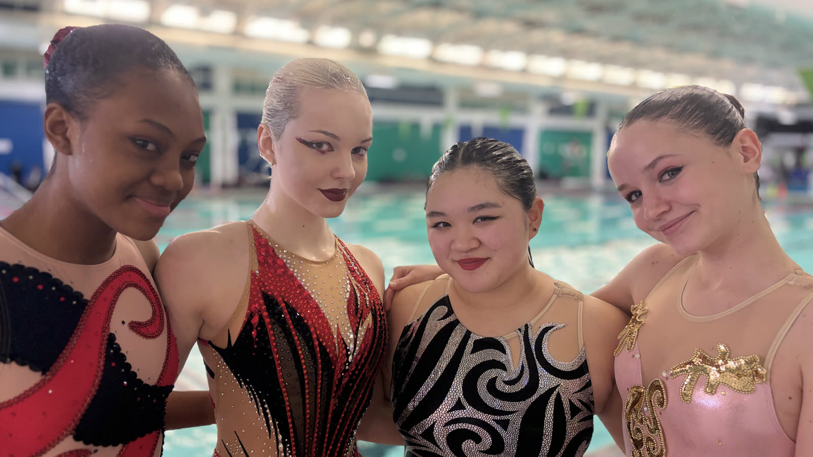 Four swimmers poolside in competition suits and full routine make-up