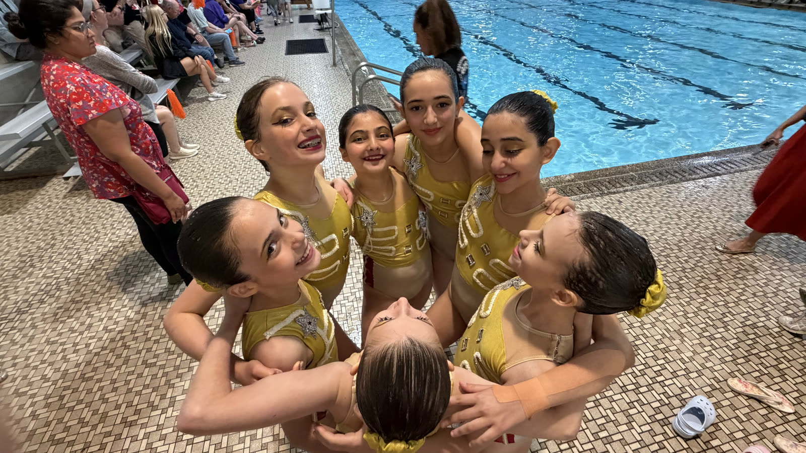 Swimmers in gold star competition suits huddled together on the deck between routines
