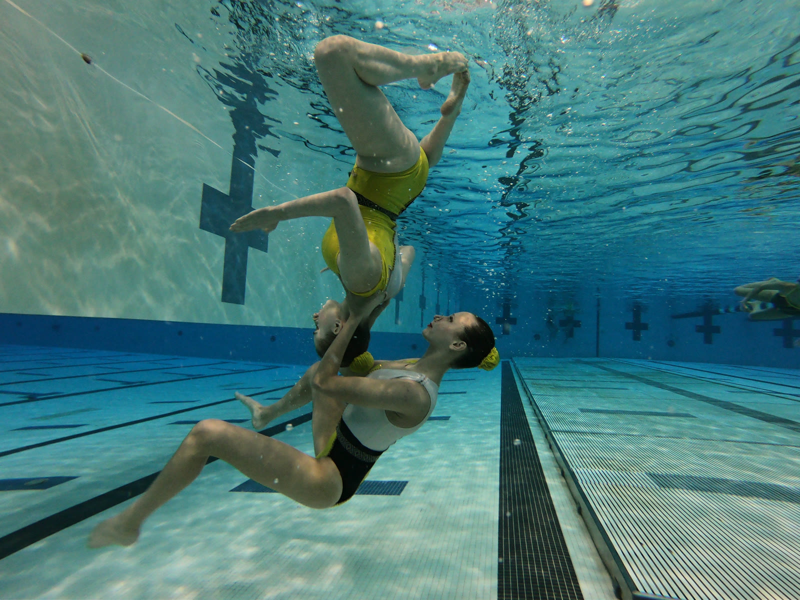 Two swimmers in gold and black suits mirroring each other underwater during a duet