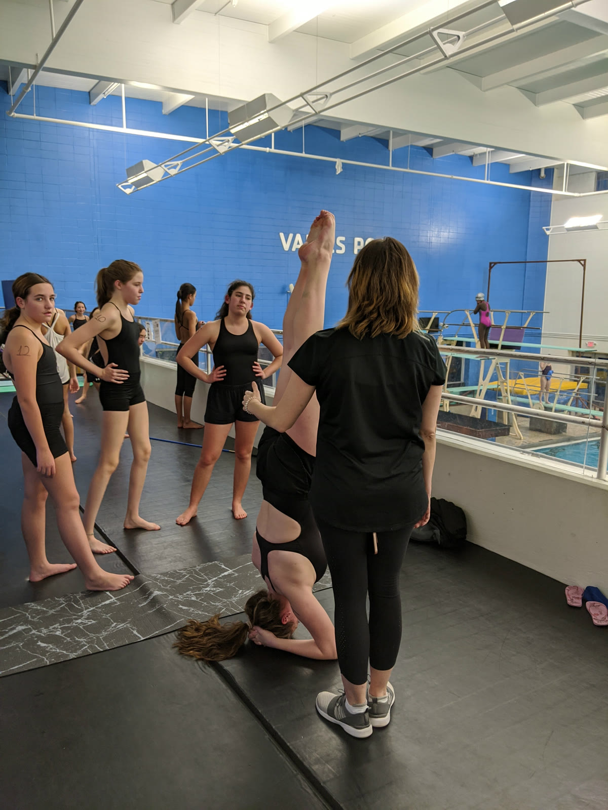 Swimmers working through a land drill on mats while a coach watches, at a USA Artistic Swimming levels test